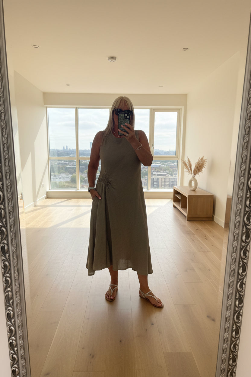 Woman taking a mirror selfie wearing a long, light-colored dress in a room with furniture.