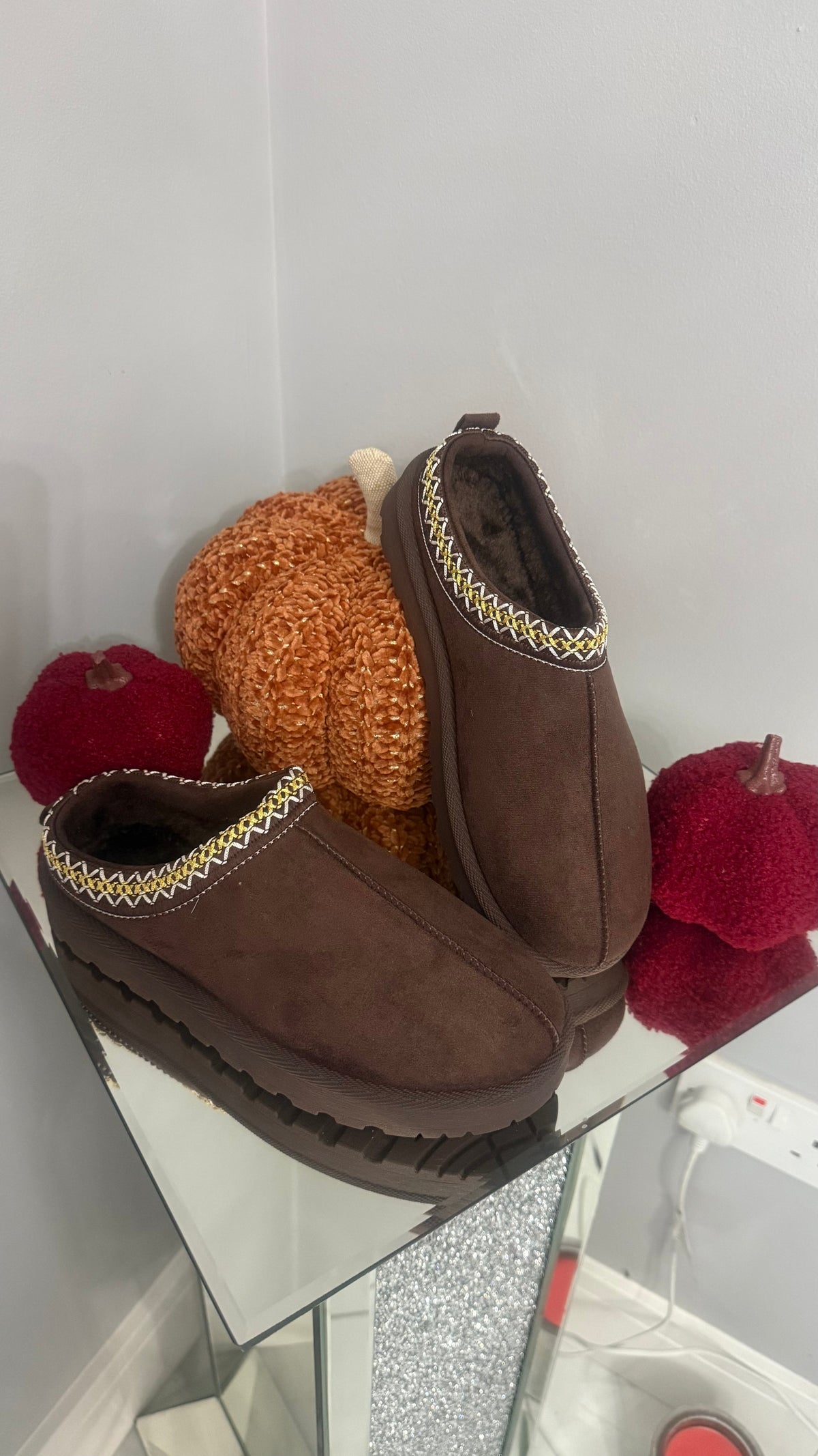 Pair of brown slippers on a glass surface with colorful pom-poms in the background.