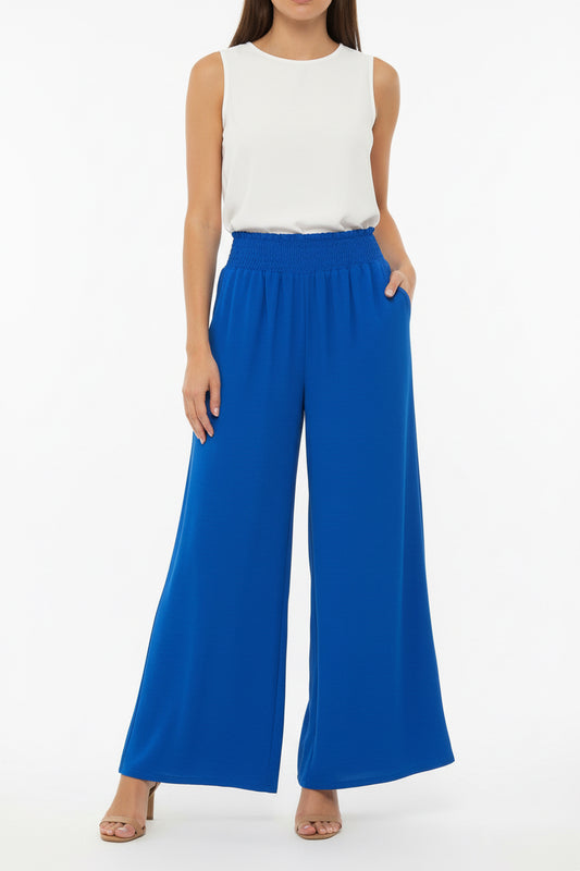 A bright royal blue maxi skirt with a smocked elastic waistband, hanging on a black hanger against a white paneled door.