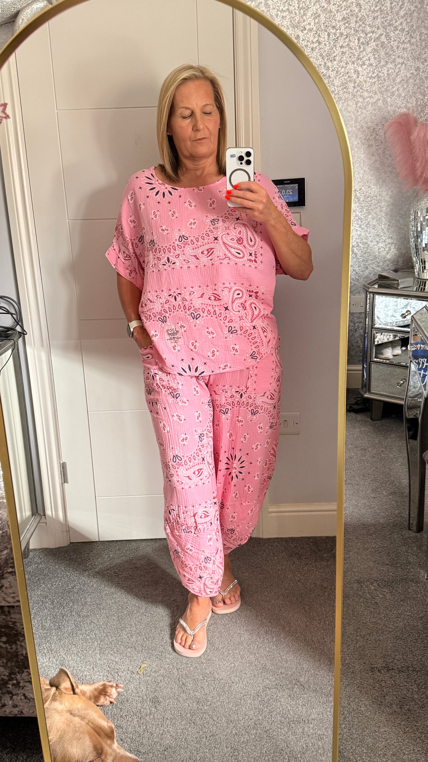Woman taking a mirror selfie wearing a pink paisley set in a room.