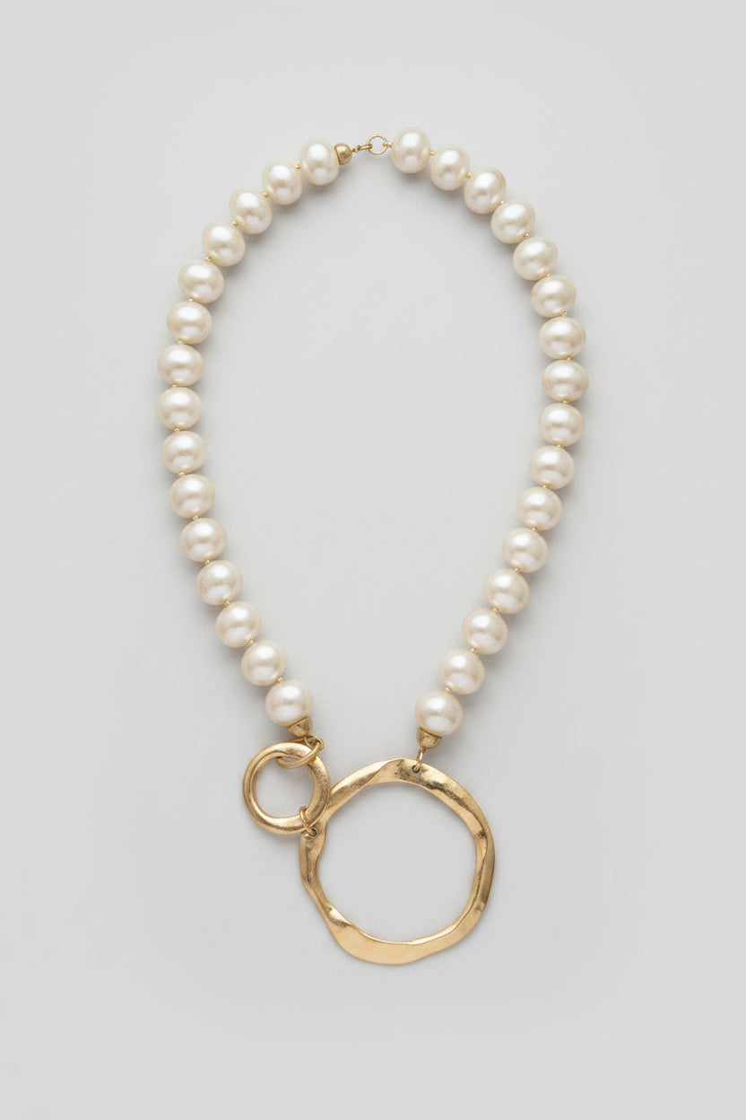 A gold and pearl beaded necklace with a hammered gold ring pendant, displayed on a white background