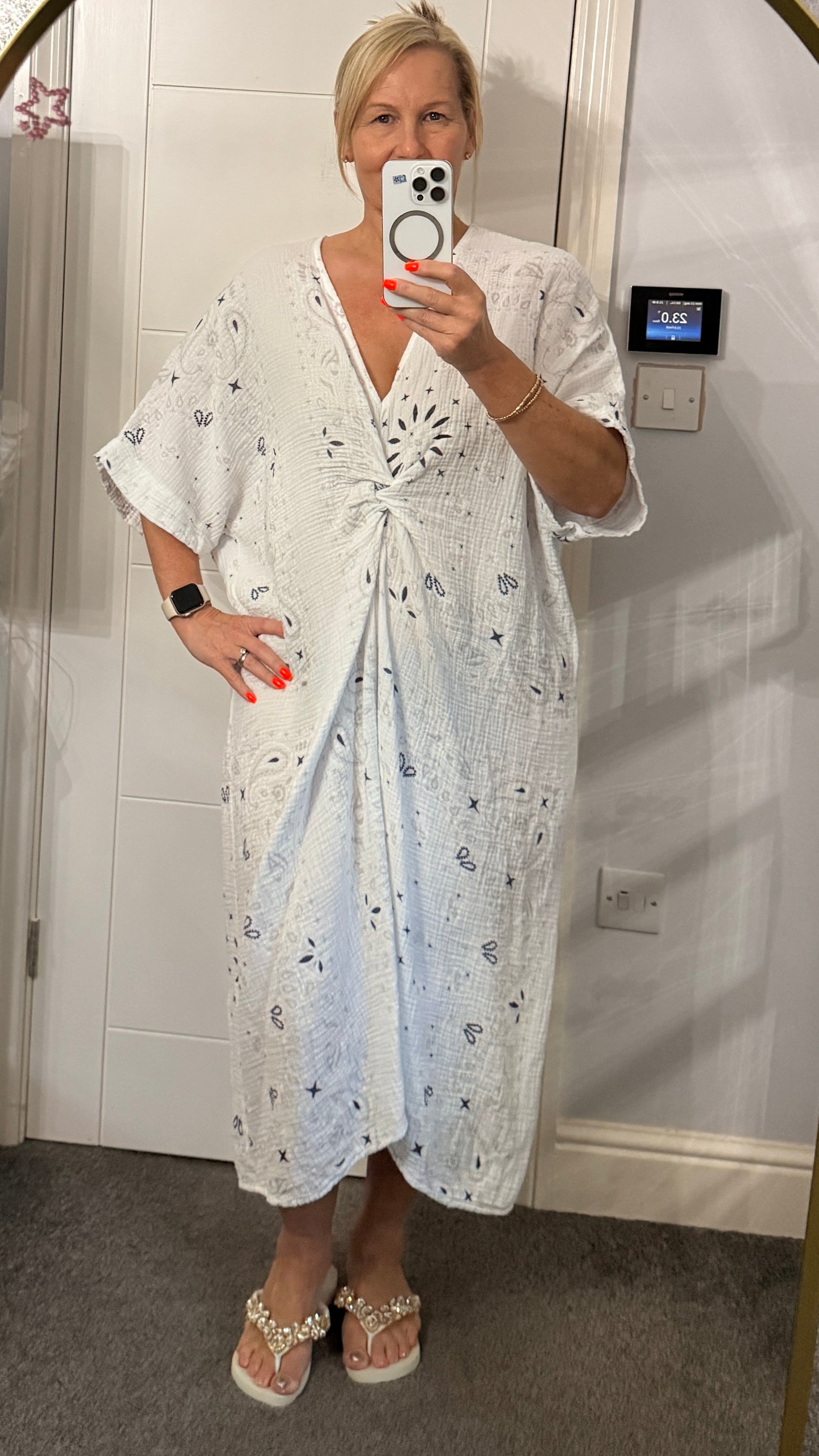 Woman taking a mirror selfie wearing a white cotton dress taking a selfie