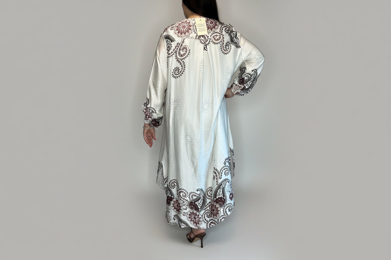 Woman wearing a long, light-colored dress with intricate patterns on a plain background
