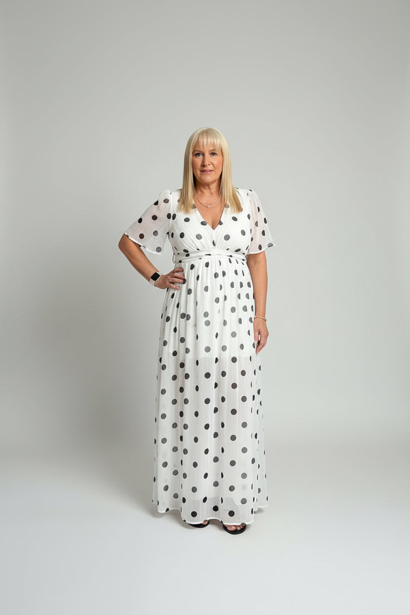 Woman in polka dot dress standing in a room with a mirror reflecting her image.