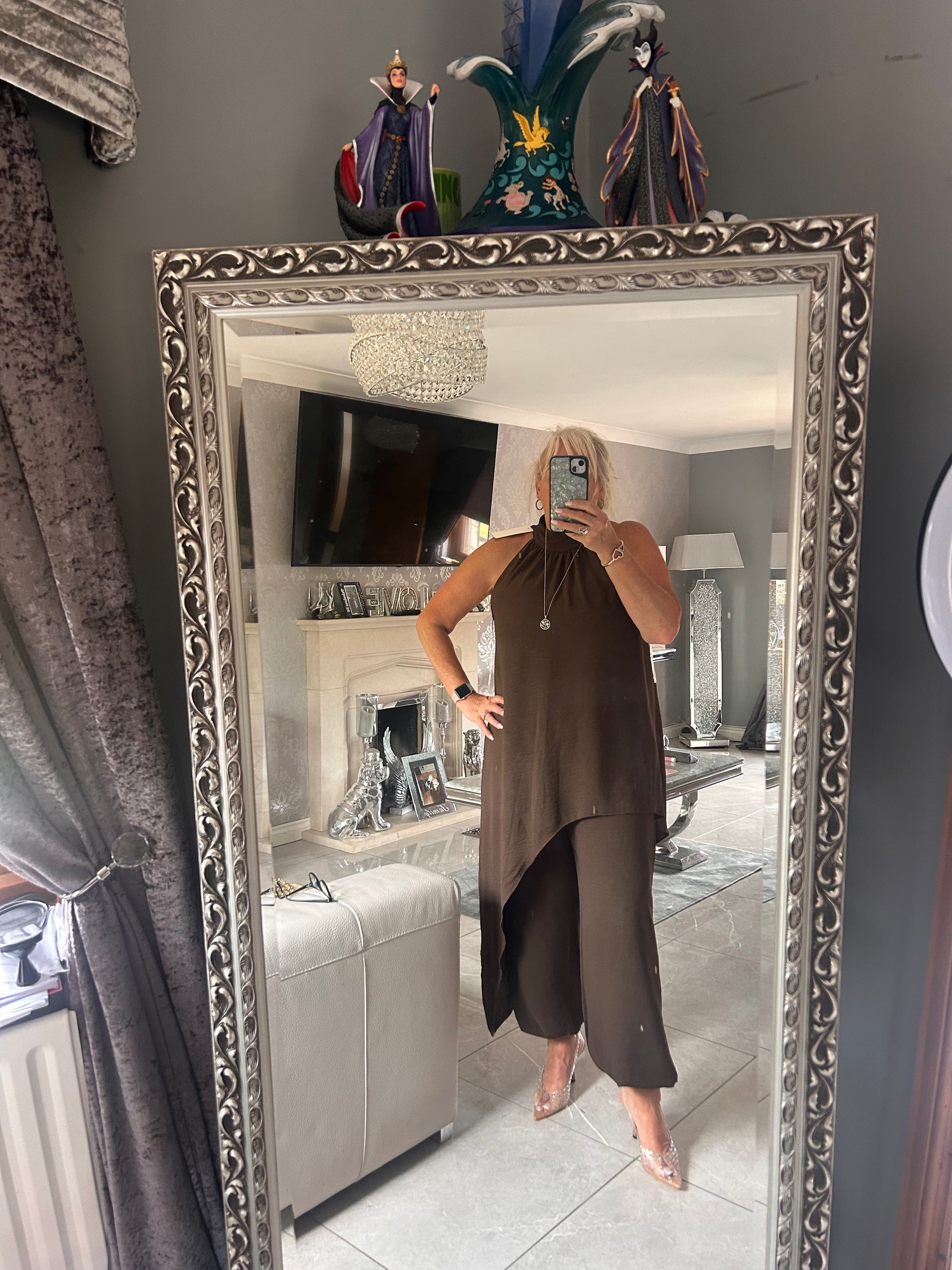 Person wearing a brown suit standing in front of a decorative mirror.