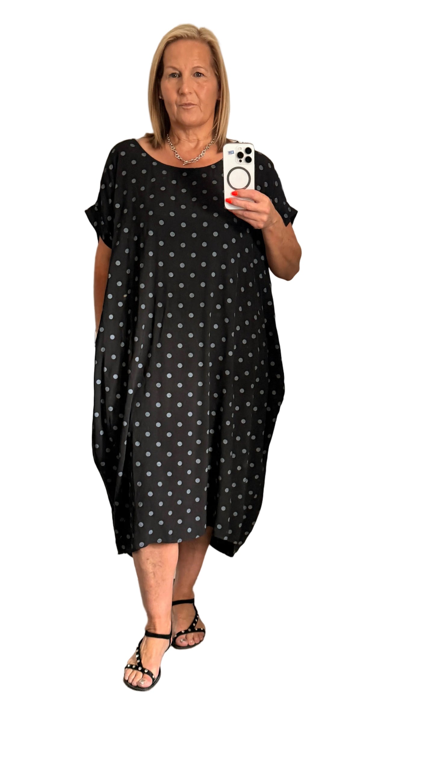 Woman wearing a black dress with white polka dots, holding a phone.