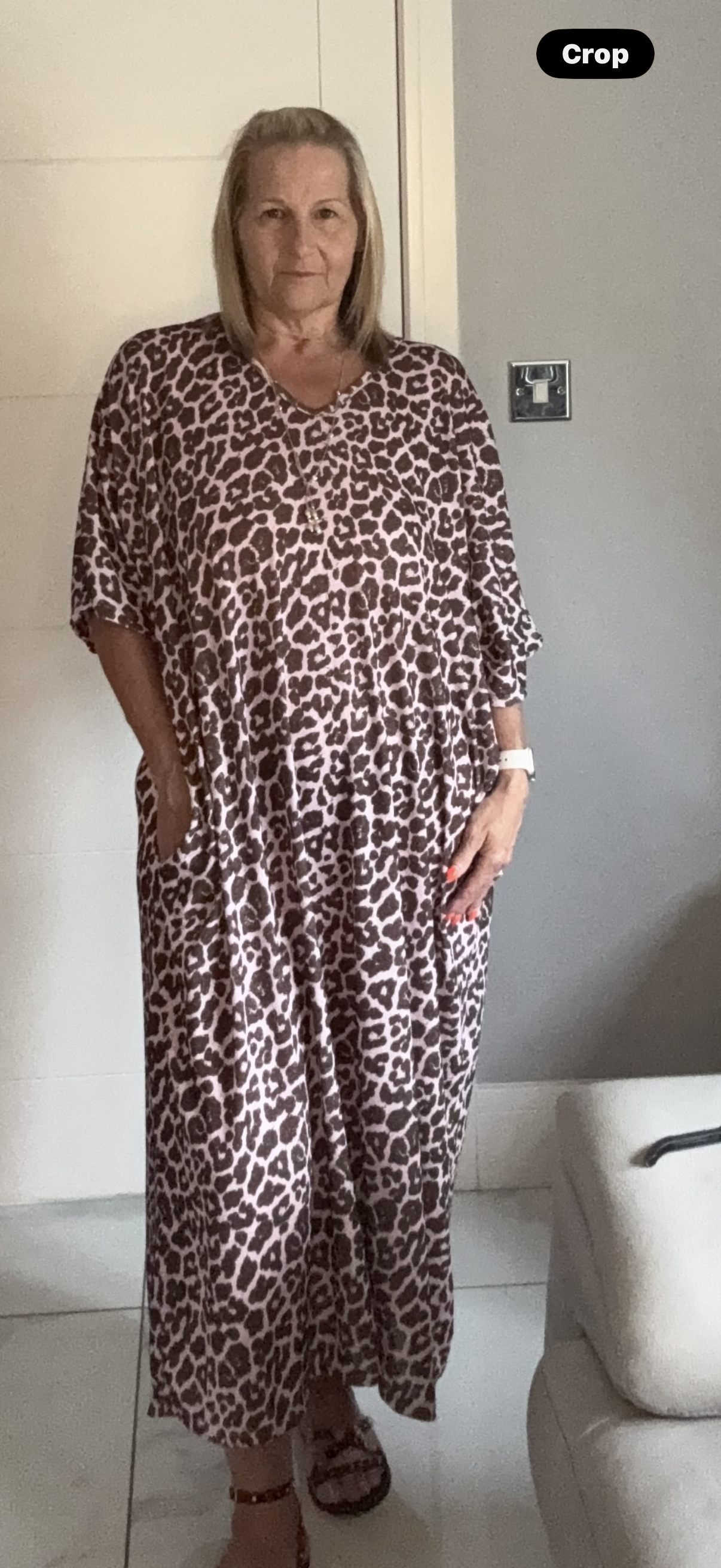 Woman wearing a leopard print dress in a room with white walls and a light-colored couch.
