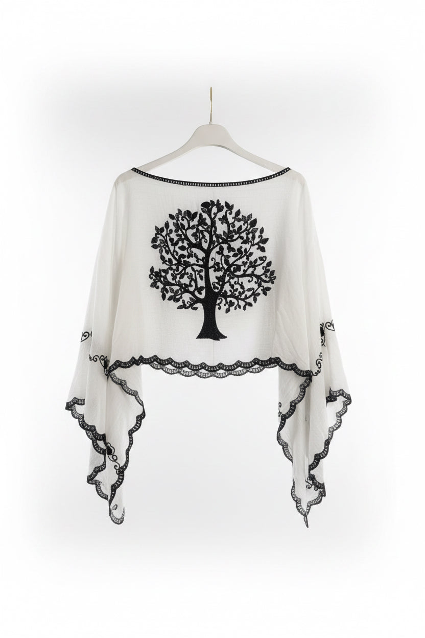 White sheer kaftan-style top with a black tree motif on the back and black lace trim, hanging on a white hanger against a white paneled door.