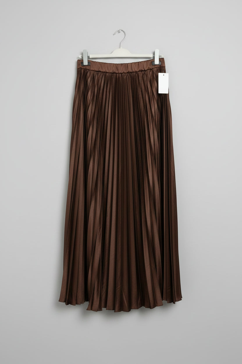 A brown pleated midi skirt hanging on a black clothes hanger against a white paneled door. A white product tag is attached near the waistband.