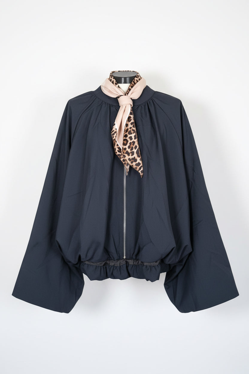 A black long-sleeve blouse with a beige and black leopard print neck scarf tied at the collar, hanging against a white paneled door.