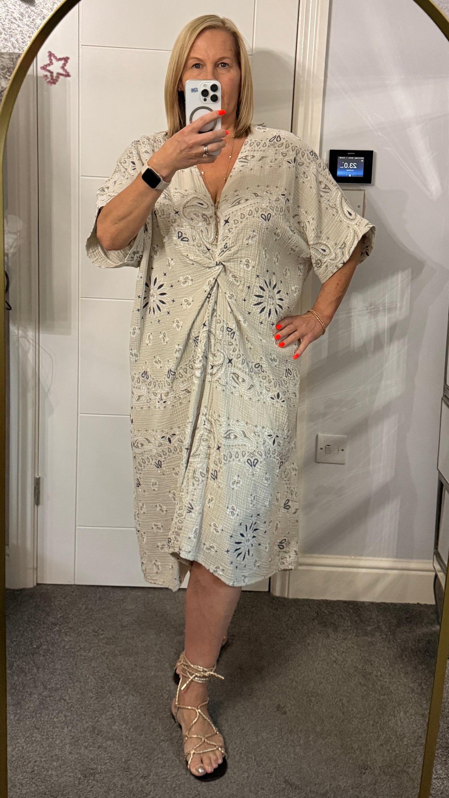 Woman wearing a light-colored dress with floral patterns in front of a mirror.