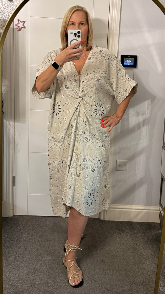 Woman wearing a light-colored dress with floral patterns in front of a mirror.