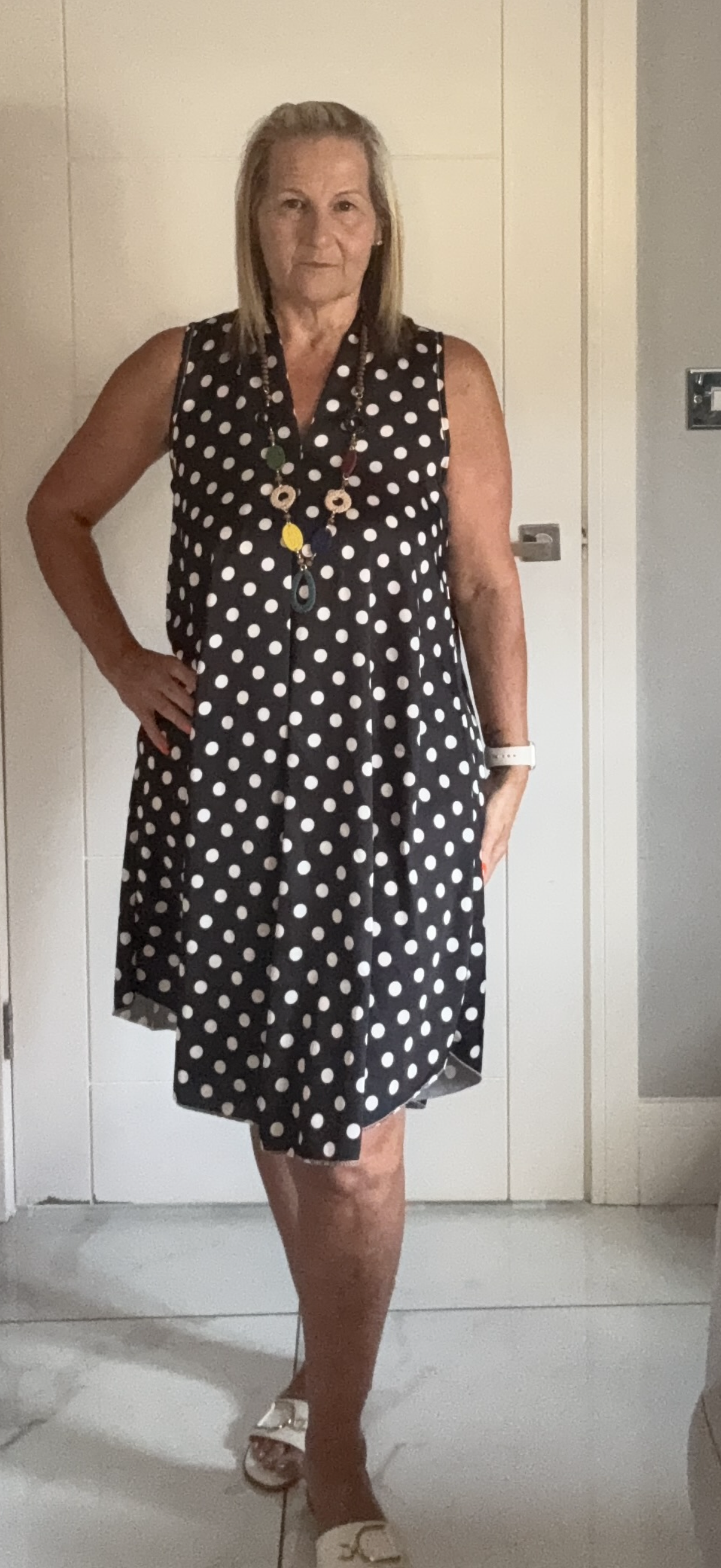 Woman wearing a black polka dot dress standing against a white wall.