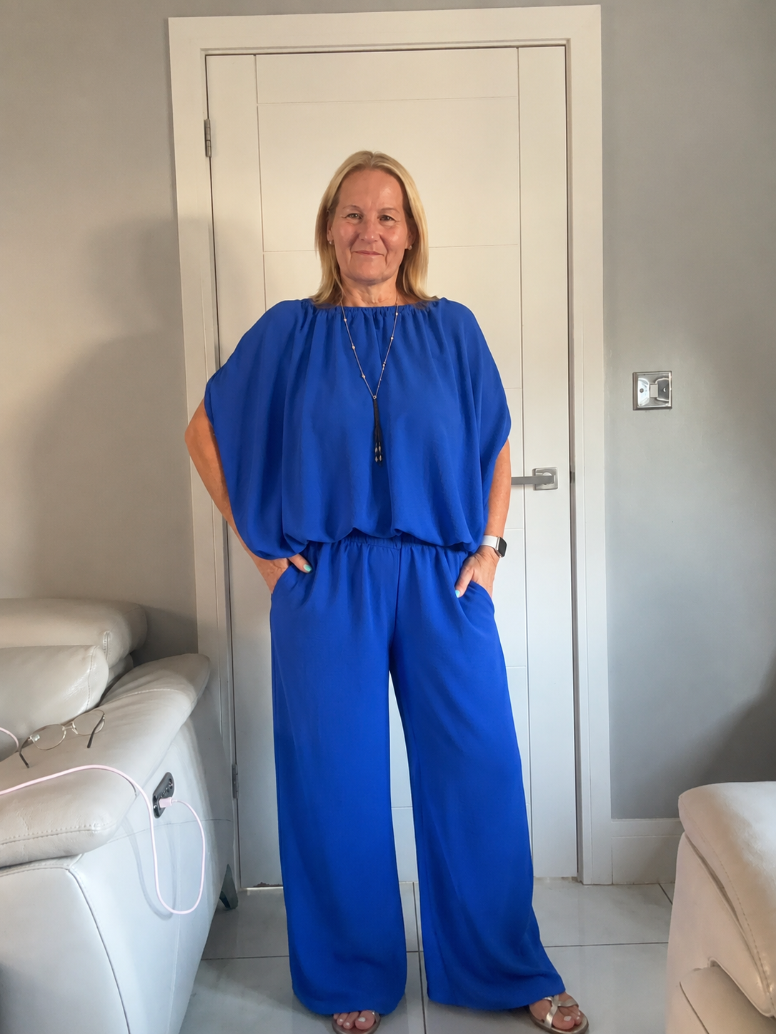 Women in royal blue suit standing in front of a white door the suit is trousers and a bubble hem top 