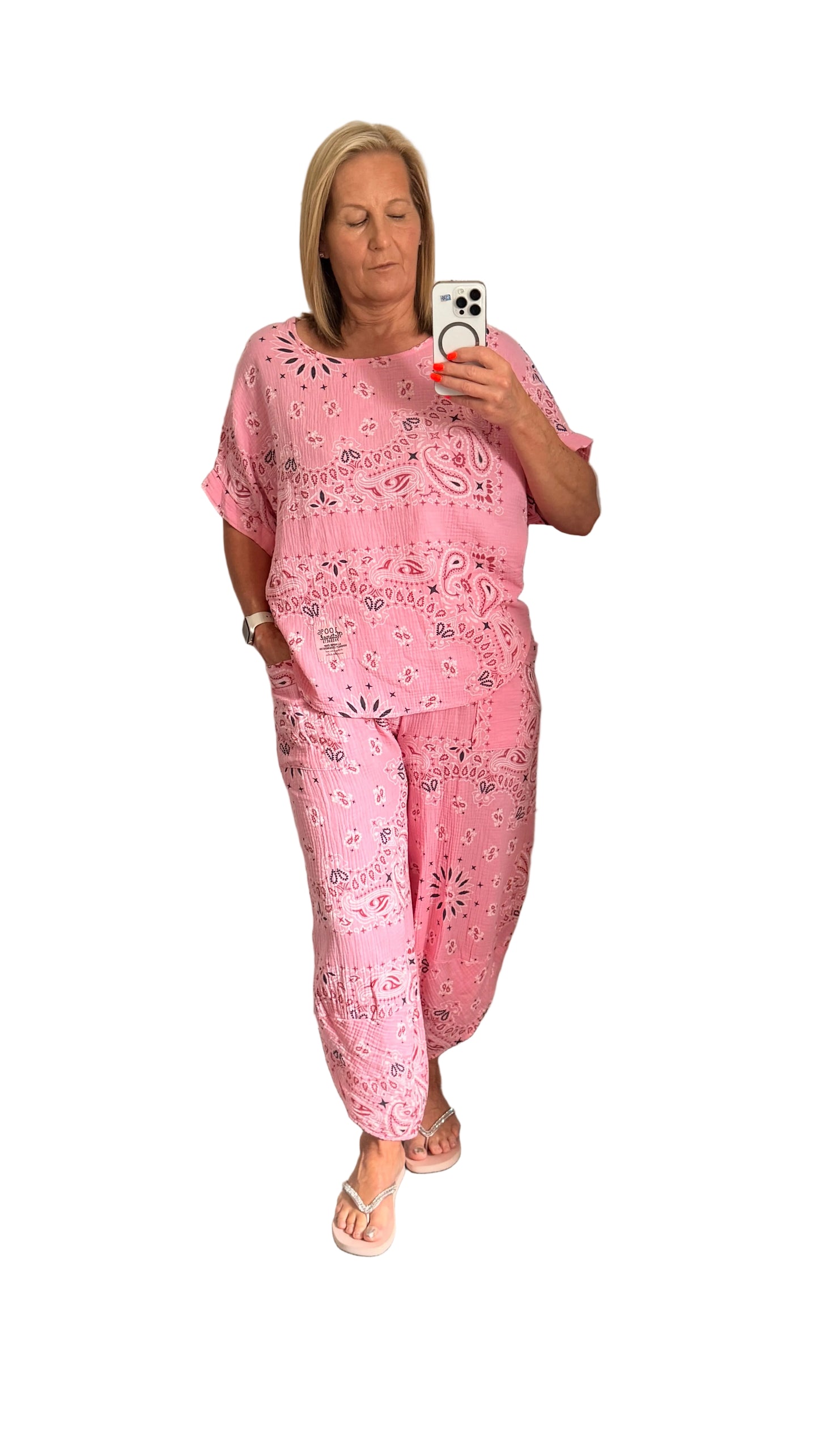 Woman taking a mirror selfie wearing a pink Paisley  set in a white  room.