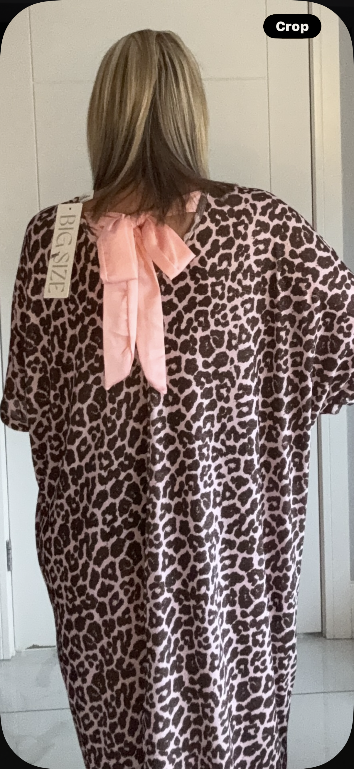Person wearing a leopard print dress with a pink bow in a neutral setting
