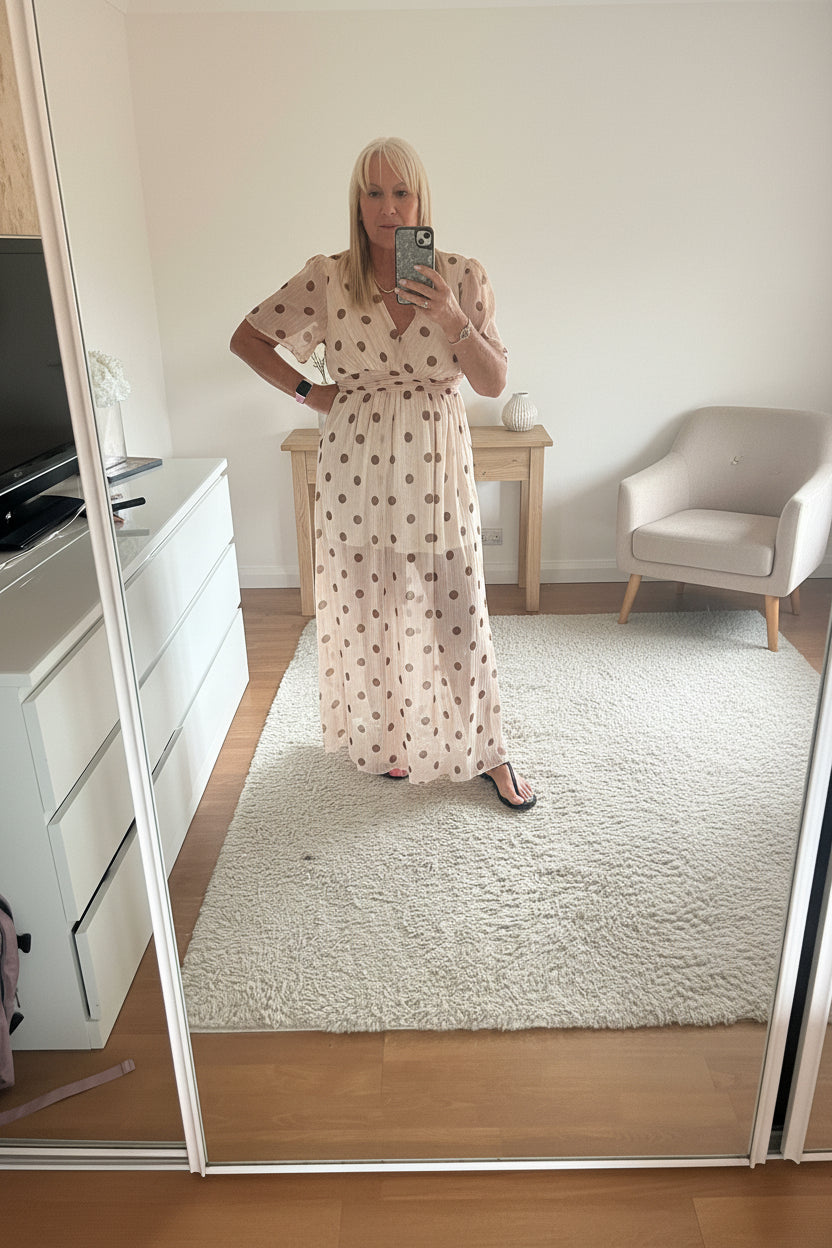 Person taking a mirror selfie in a room with a window and furniture wearing the dotty dress