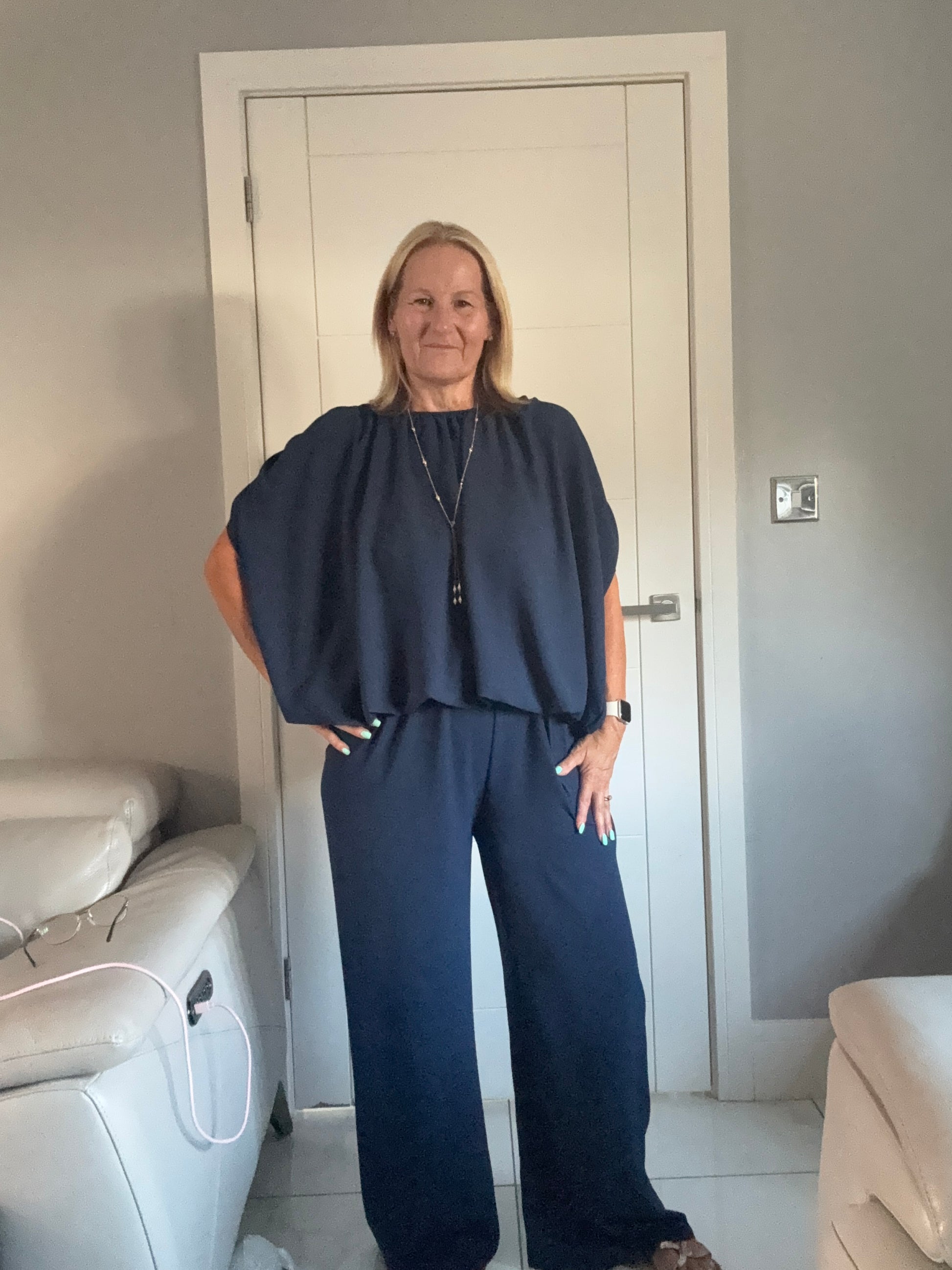 Women in navy blue suit standing in front of a white door the suit is trousers and a bubble hem top 