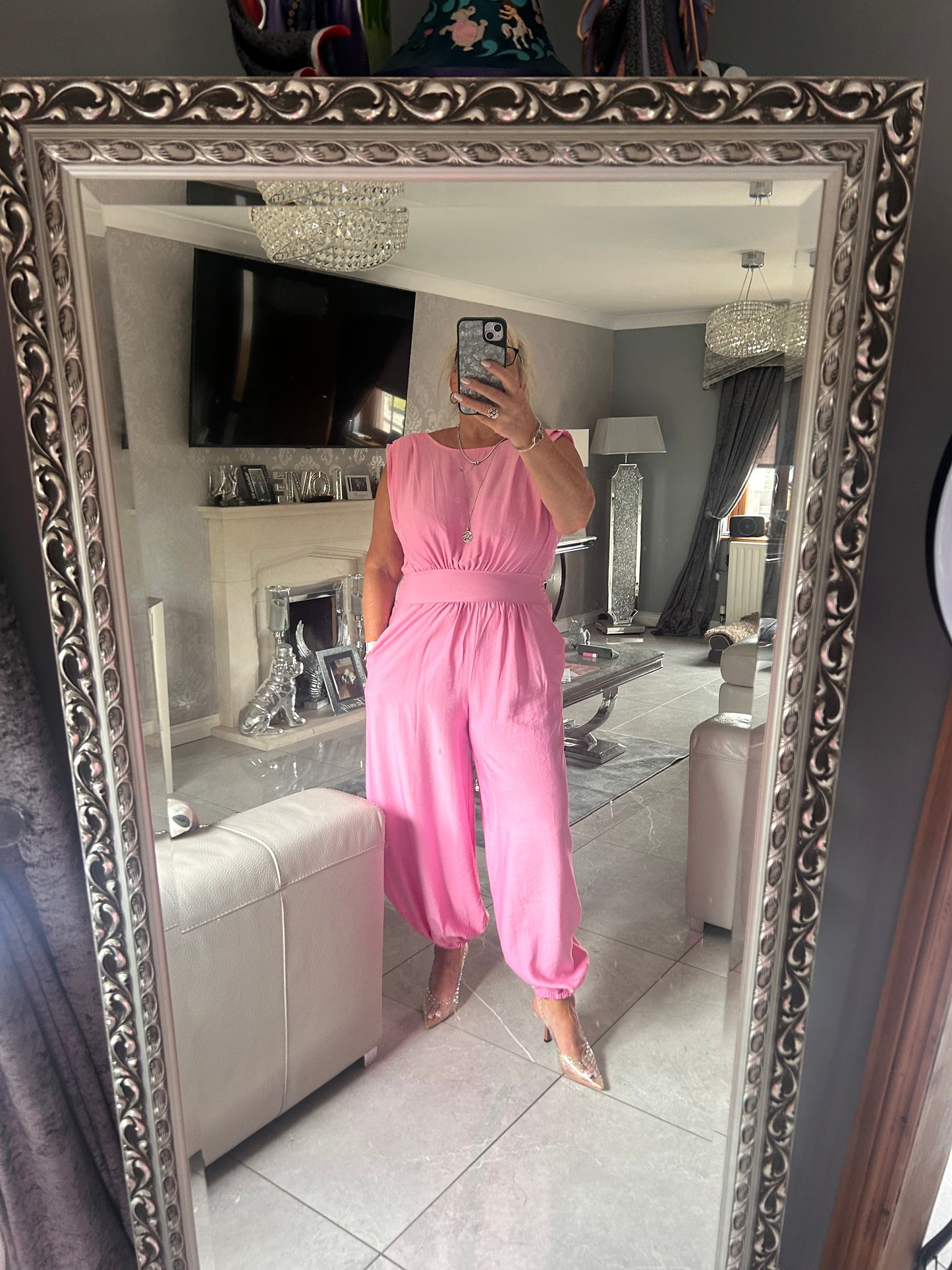 Person wearing a pink jumpsuit standing in front of a decorative mirror.