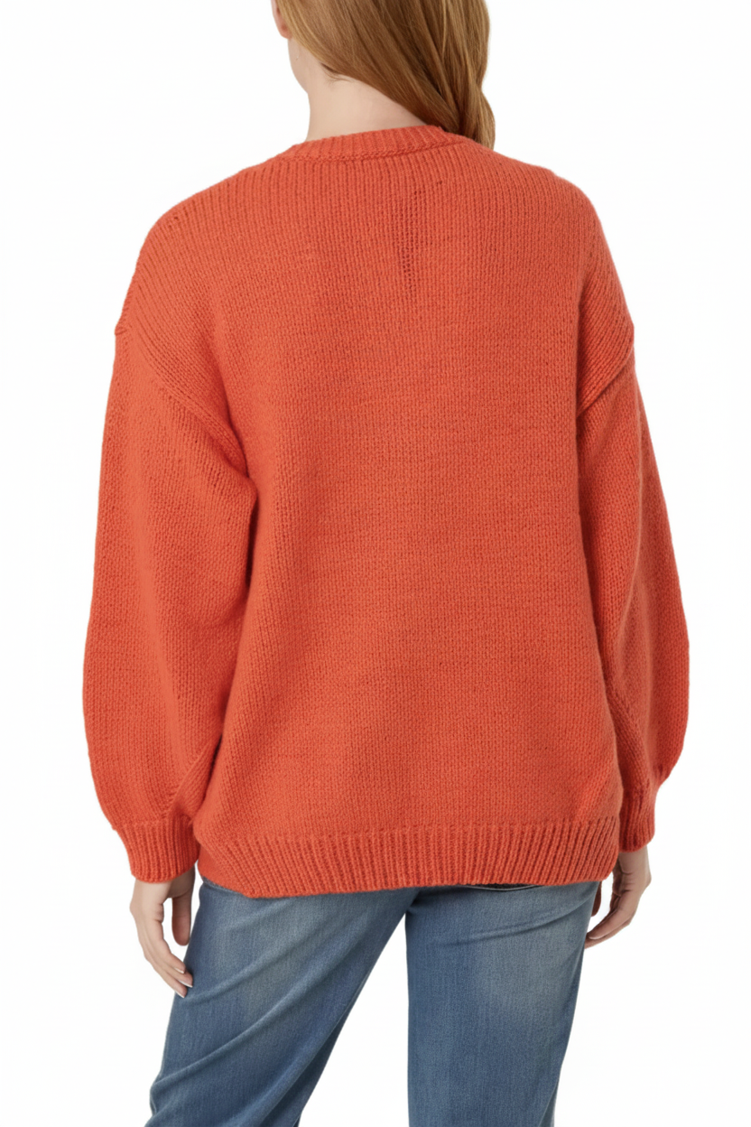 A woman viewed from the back wearing a loose  coral daisy knit sweater and blue jeans against a plain white background.