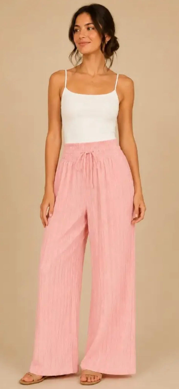 Woman wearing a white tank top and pink wide-leg pants on a beige background