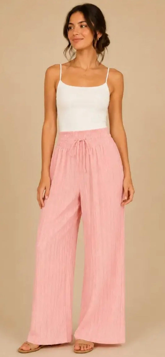 Woman wearing a white tank top and pink wide-leg pants on a beige background