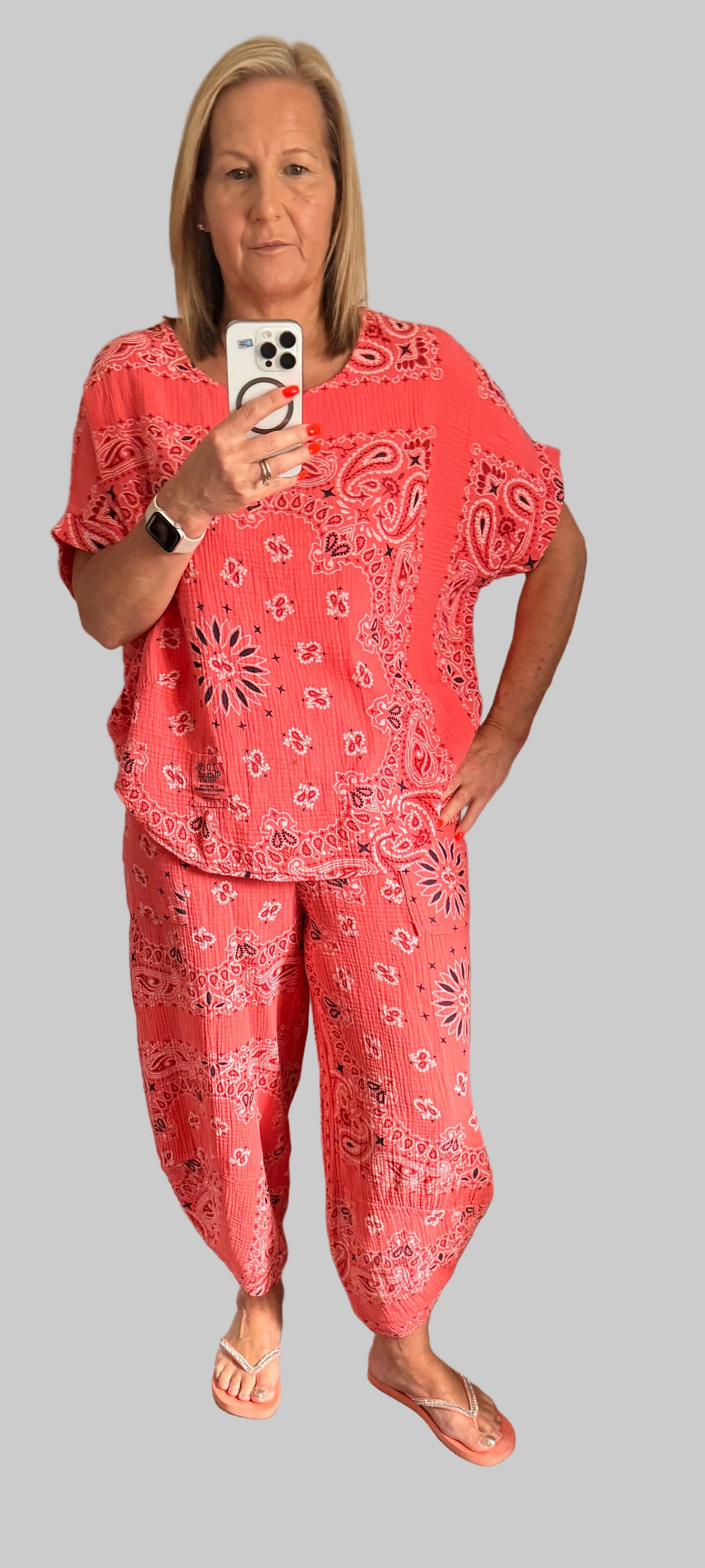 Woman wearing a Coral  paisley suit taking a selfie on a grey background