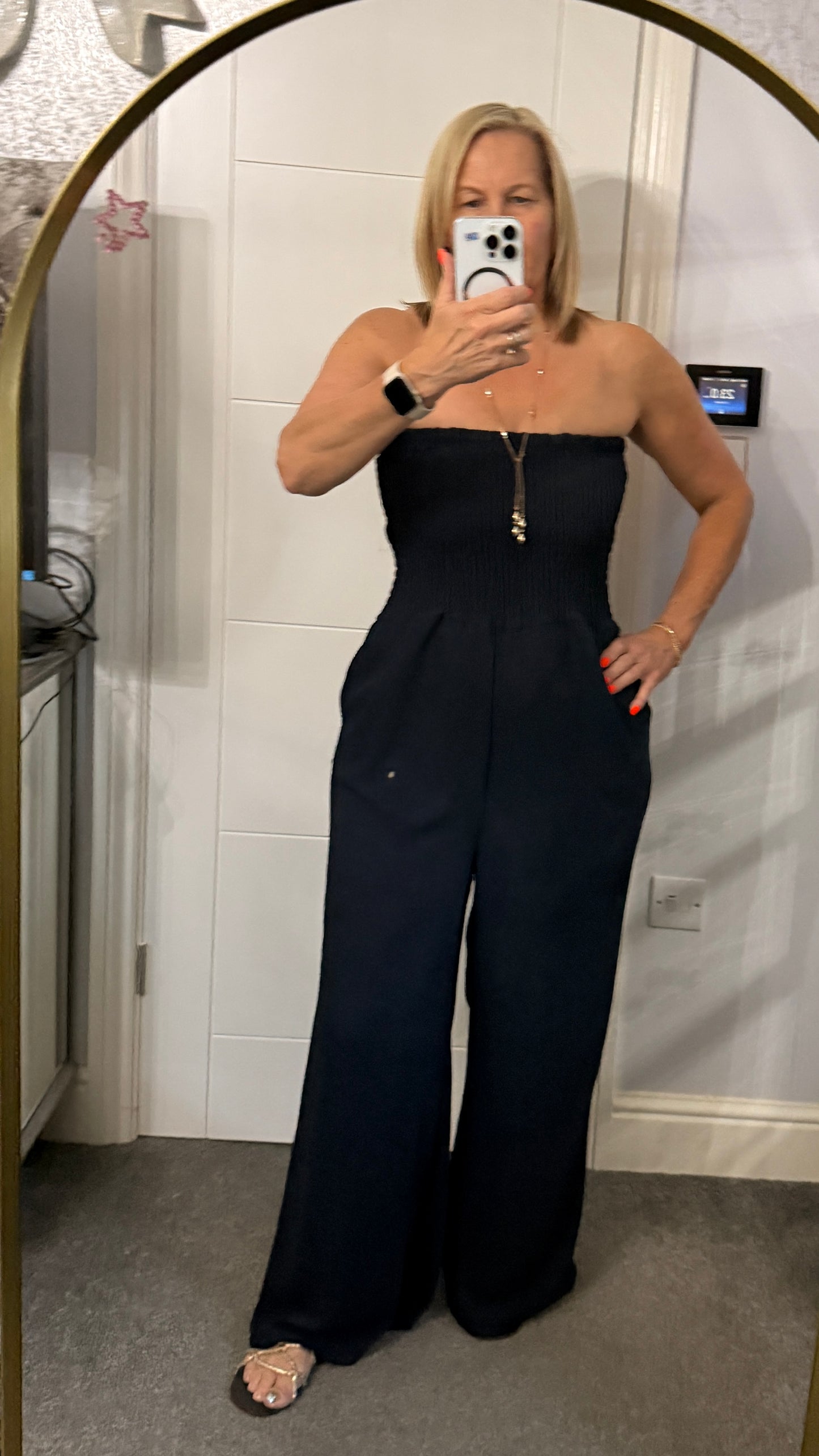 Person wearing a black strapless jumpsuit taking a mirror selfie.
