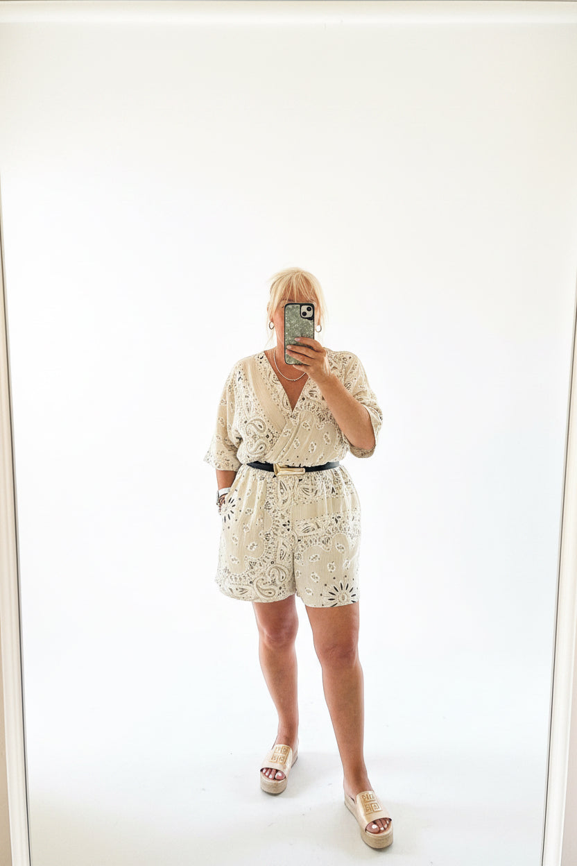 Person wearing a beige Millie play suit taking a mirror selfie on a plain background