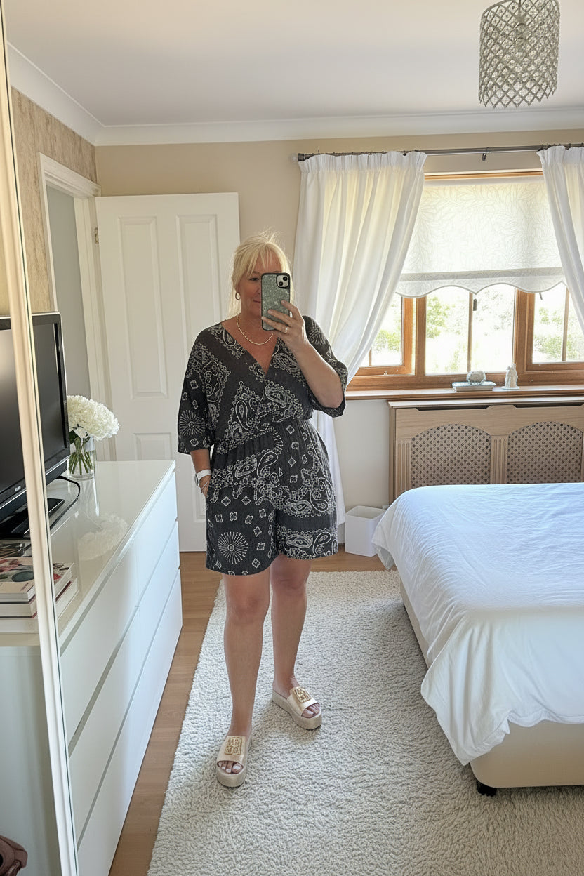 Woman taking a mirror selfie in a bedroom with a bed and window in the background.
