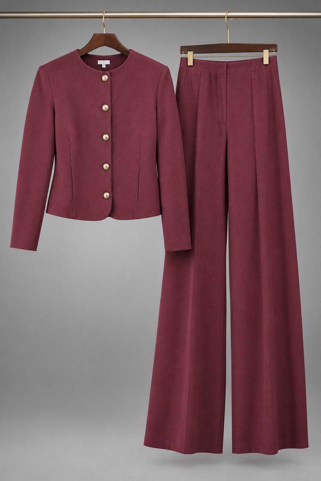 A two-piece women's suit set in a deep burgundy/maroon color, featuring a cropped long-sleeve cardigan with decorative gold-tone buttons and matching wide-leg trousers, displayed on hangers against a white paneled door.