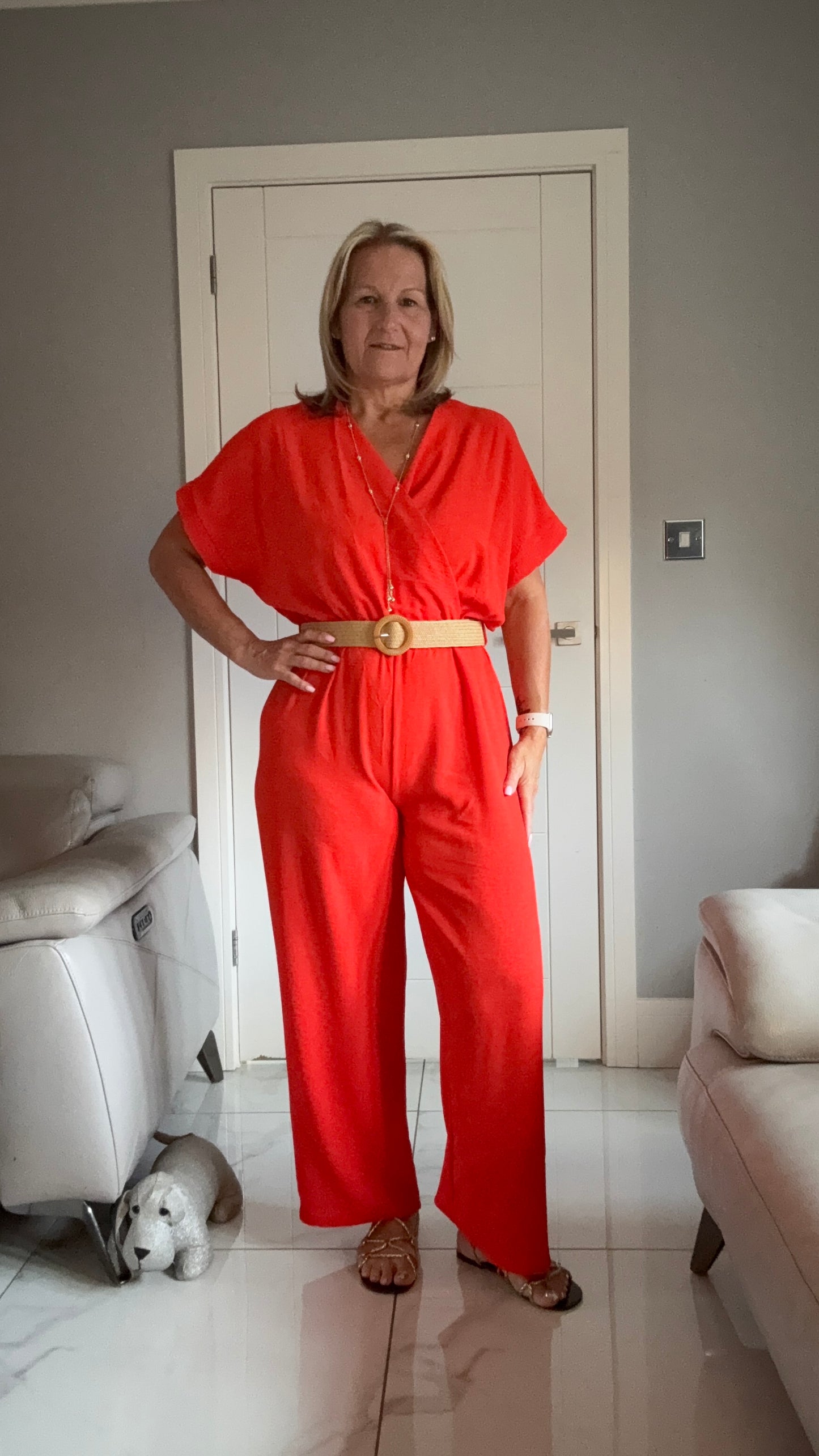 Woman in a red jumpsuit standing in a room with white furniture and a dog.
