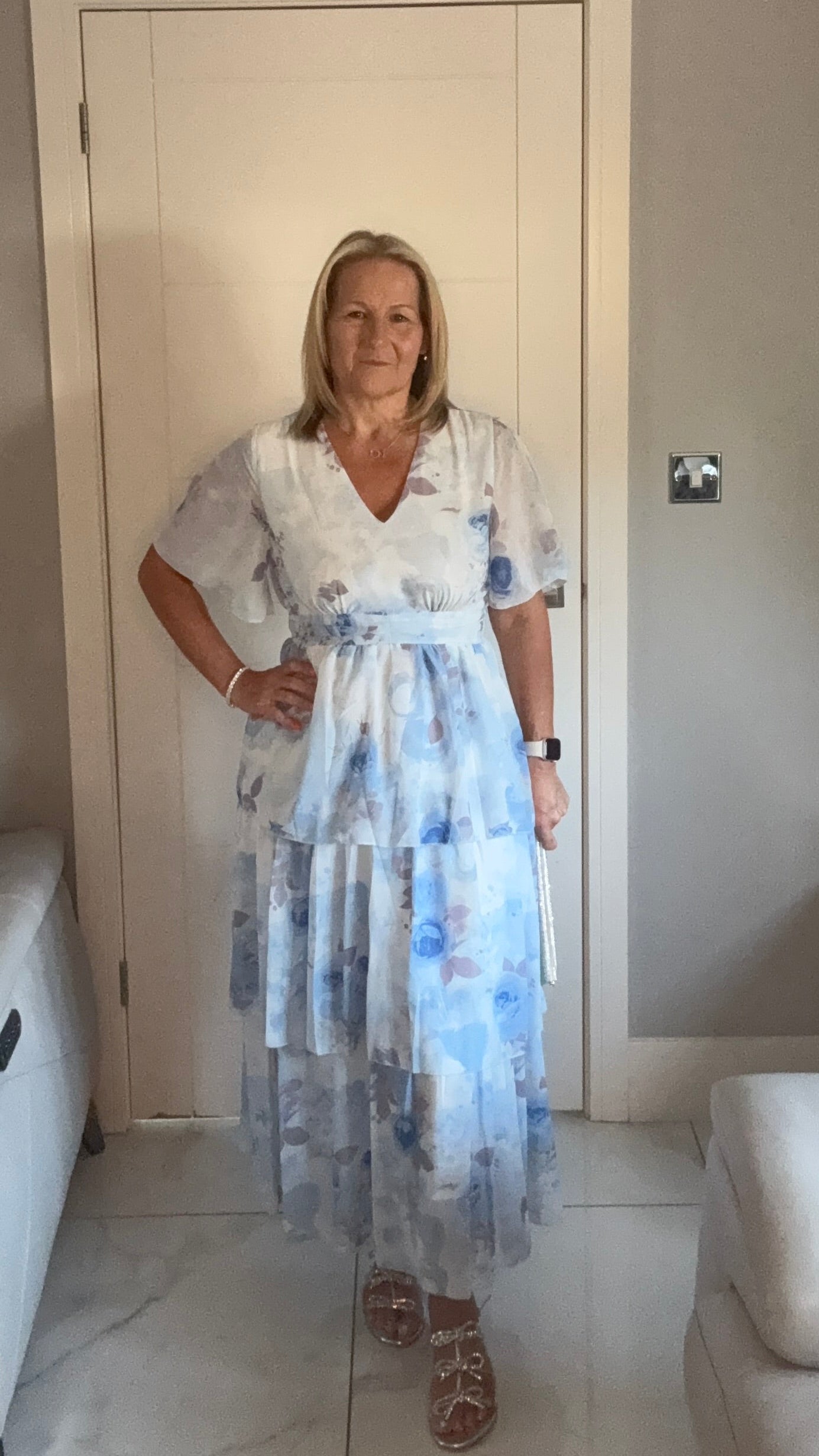Woman wearing a floral dress standing in a room with a white door and light-colored walls.