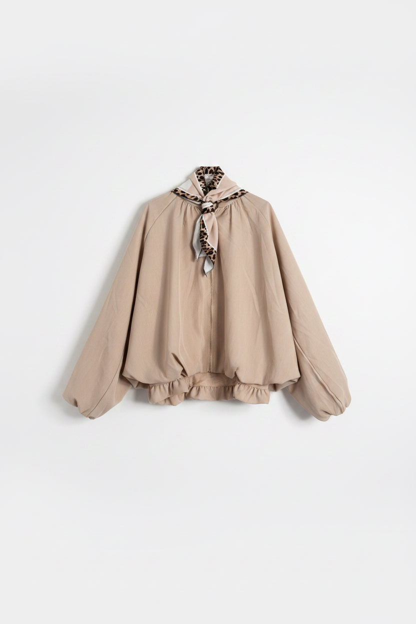 A beige long-sleeve blouse with a ruffled hem and a leopard-print neck scarf tied at the collar, hanging on a white paneled door.