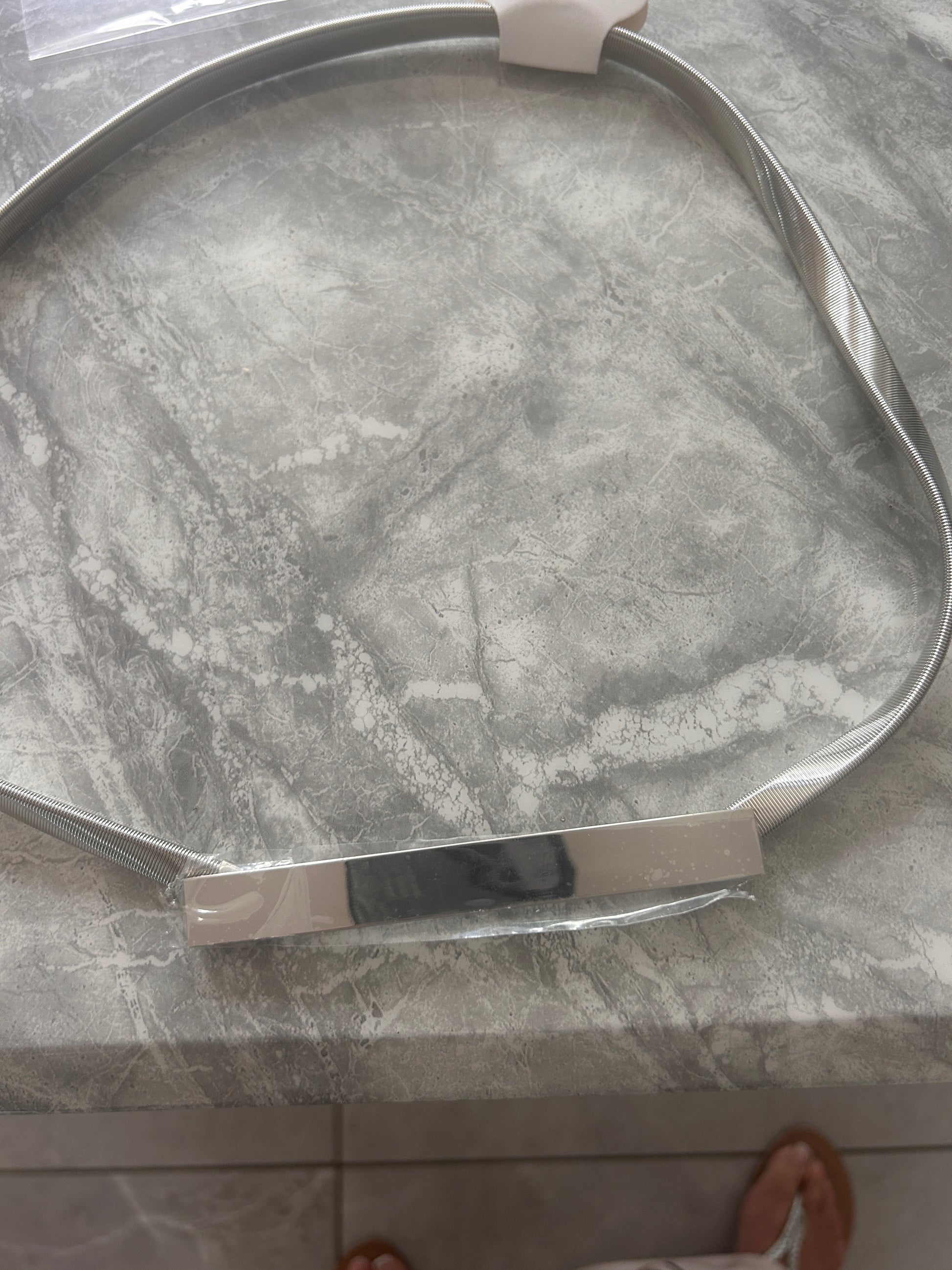 A silver stretchy Belt with a clear plastic wrap, placed on a Gray marble-patterned  table top