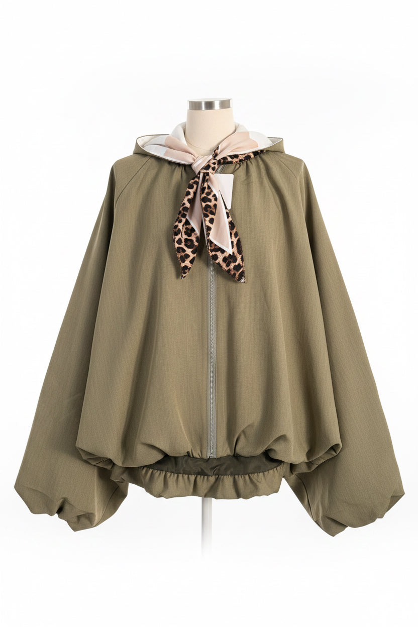 A khaki long-sleeve zip-up jacket with a beige and leopard-print neck scarf, hanging on a white paneled wall.