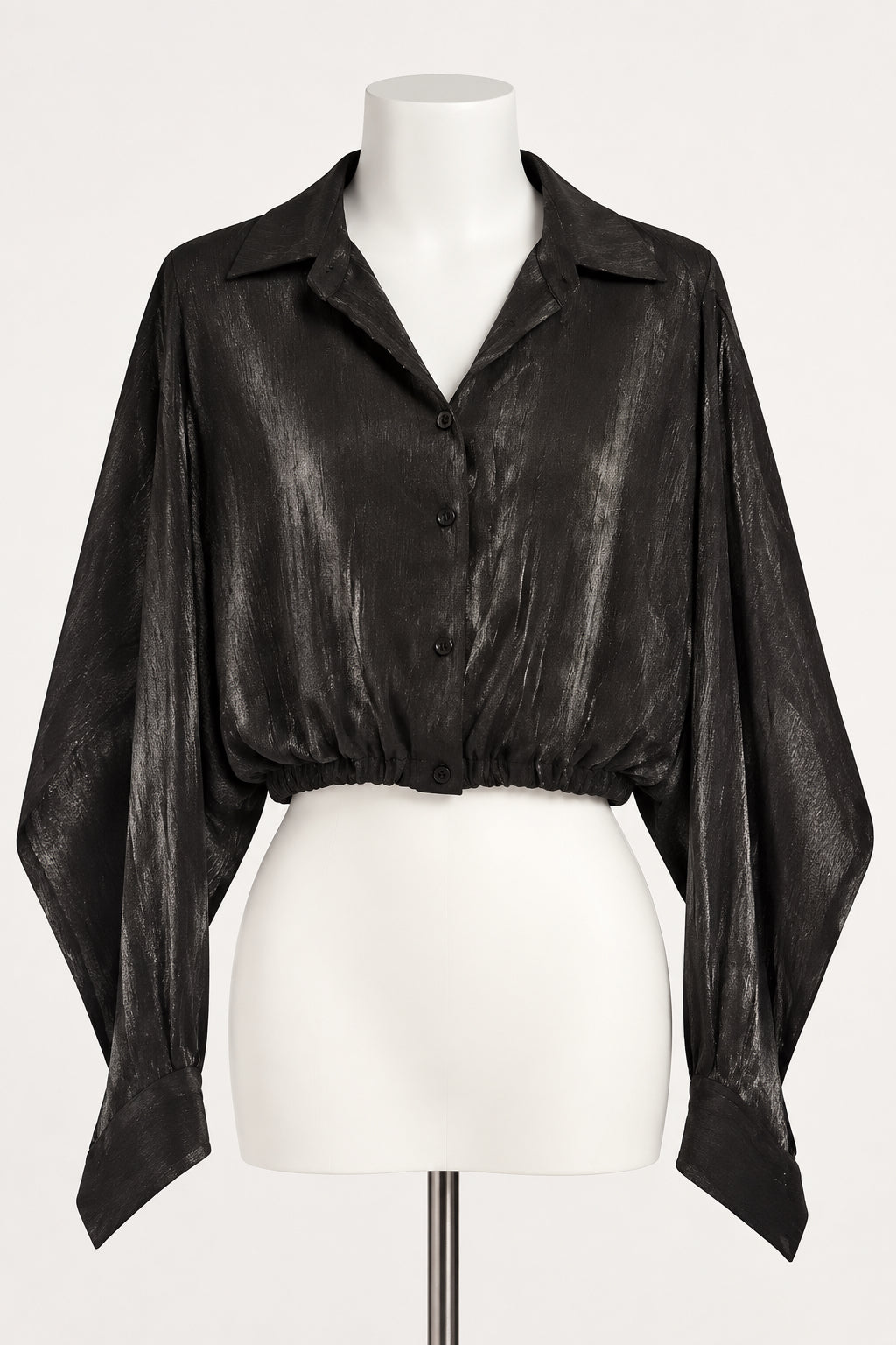 A black long-sleeve button-up shirt with a metallic, crinkled texture, hanging on a black hanger against a white paneled wall.