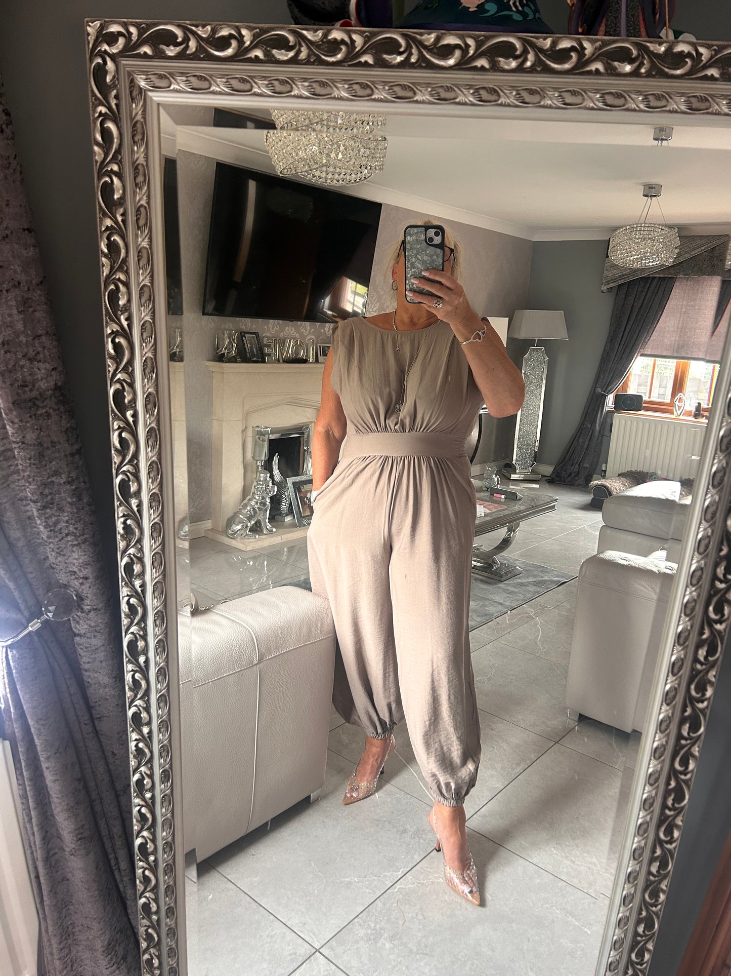 Person wearing a long, light-coloured jumpsuit standing in front of a decorative mirror.
